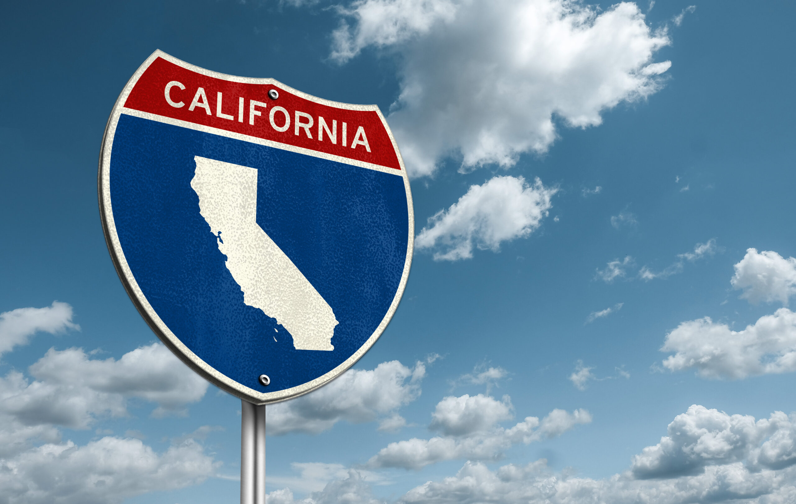 A road sign with the word "California" at the top in white text on a red background, above a white outline of the State on a blue background. Beyond the sign, is a blue sky with a spattering of clouds.